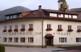 Hausansicht, © Gruber Johann Ein traditionelles Gasthaus mit Blumen an den Fenstern und einem Kirchturm im Hintergrund.