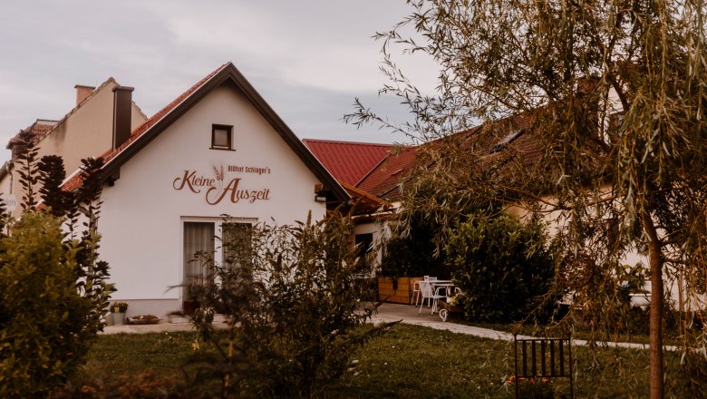 Biohof Schlager in Mollram, © Haberler Photografie Ein kleines Gebäude mit der Aufschrift 'Biohof Schlager's Kleine Auszeit', umgeben von Bäumen und Gartenmöbeln.