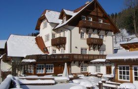 Der Althammerhof im Winterkleid, © Althammerhof, Julius Schneidhofer Ein großes, traditionelles Haus im Schnee mit Holzverzierungen und blauen Himmel im Hintergrund.