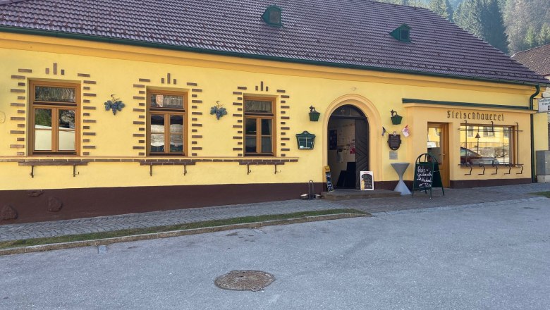 Gasthaus Haselbacher, © Wiener Alpen Gelbes Gebäude mit der Aufschrift 'Fleischhauerei' und einem Eingang.