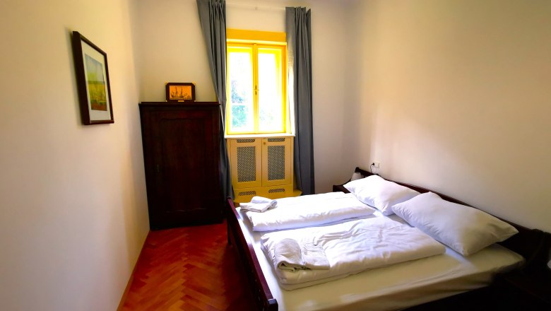 Schlafzimmer im Appartement Henriette, © Herrnhof Schlafzimmer mit Doppelbett, Schrank und Fenster mit gelbem Rahmen.
