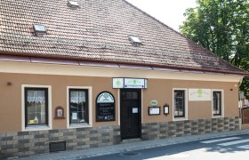 Das Haus stammt aus dem Jahr 1650, © Niederösterreich Werbung/Nadja Büchler Historisches Gebäude mit brauner Fassade und Schildern. Es hat ein Ziegeldach und Fenster mit Gardinen.