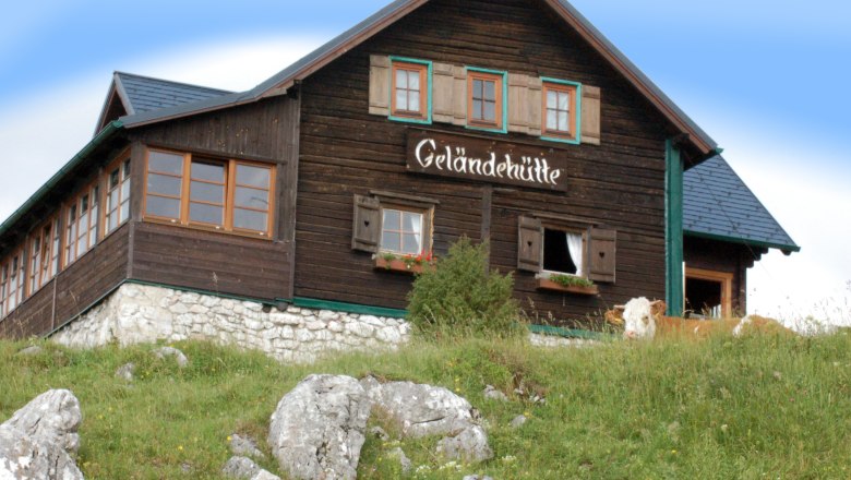 Geländehütte, © Gelaendehuette, Foto Fam. Postl Eine Berghütte mit der Aufschrift 'Geländehütte' auf einer Wiese mit Felsen und einer Kuh im Vordergrund.