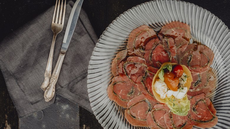 Rustikales Ambiente, idyllischer Lage, hochwertige Küche, © Niederösterreich Werbung/Rita Newman Ein Teller mit dünn geschnittenem Fleisch und einer kleinen Salatgarnitur in der Mitte, daneben Besteck auf einer Serviette.