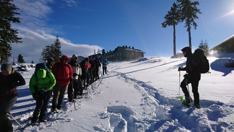 Schneeschuhwandern mit Teamwandern, © Wolfgang Menzel Gruppe von Menschen beim Schneeschuhwandern in verschneiter Landschaft mit Berghütte im Hintergrund.