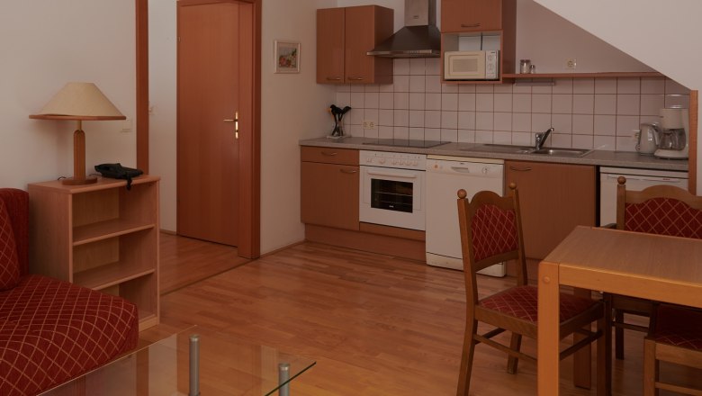 Küche, © Landhaus Puchbergerhof by smc Kompakte Küche mit Holzschränken, Esstisch und Stühlen, Herd, Spüle und Mikrowelle.