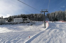 Direkt an der Skipiste, © Alpengasthof Fernblick, Fam. Pölzelbauer Schneebedeckte Skipiste mit Skilift und Wald im Hintergrund.
