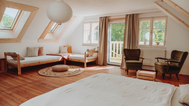 Mehrbettzimmer, © Sabrina Stummer Helles Mehrbettzimmer mit Holzboden, zwei Betten, zwei Sesseln und großen Fenstern.