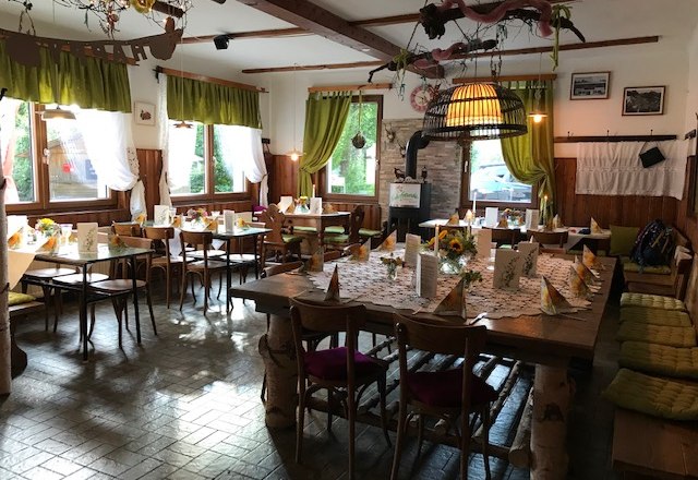 Innenraum, © Waxeneckhaus Gemütlicher Gastraum mit Holzmöbeln, dekoriert mit Blumen und Tischdecken.