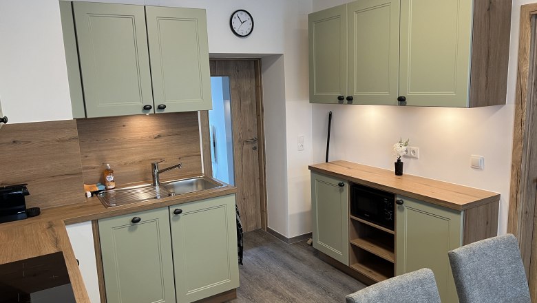 Küche Ferienhaus Höflein, © Anton Sommer Moderne Küche mit grünen Schränken, Holzarbeitsplatten und grauen Stühlen.