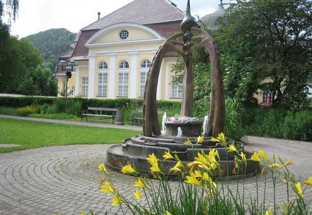 Pernitz, Pfarrheim, © Marktgemeinde Pernitz, Foto privat Brunnen vor einem historischen Gebäude mit gelben Blumen im Vordergrund.