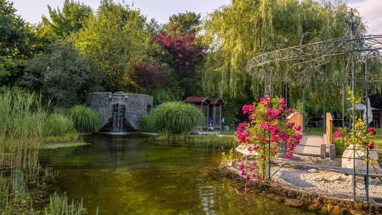 Naturhotel Molzbachhof, © Niederösterreich Werbung / Maximilian Pawlikowsky Ein idyllischer Garten mit einem Teich, Wasserfall, Brücke und blühenden Blumen im Naturhotel Molzbachhof.