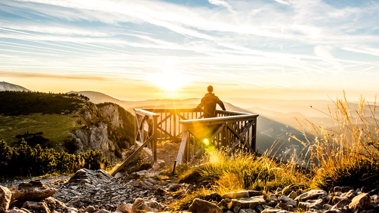 Ottohaus lookout, © Niederösterreich-Werbung/ Robert Herbst Person stands on a wooden platform and gazes into the sunset over a mountain landscape.