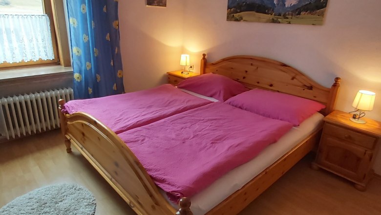 Doppelzimmer, © Martin Zwinz Gemütliches Doppelzimmer mit Holzbett, pinker Bettwäsche und Nachttischen mit Lampen.