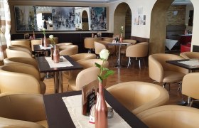 Stadtcafé Gloggnitz, © Stadtcafé Gloggnitz Innenansicht eines stilvollen Cafés mit beigen Sesseln und dekorativen weißen Blumen an der Decke.