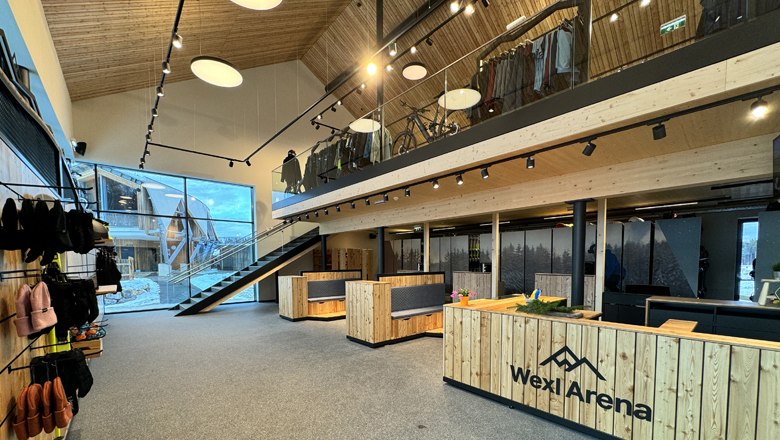 "Wexl Base" - Servicezentrum, Winter-Outdoorschule, Verleih und Shop, © Wexl Arena St. Corona am Wechsel Innenansicht des Wexl Base Servicezentrums mit Holzmöbeln und einer Treppe.