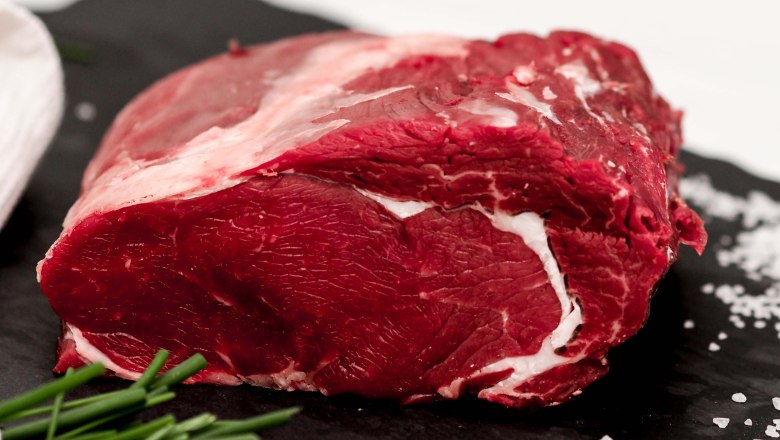 Rindfleisch, © Anni Putz Ein rohes Stück Rindfleisch liegt auf einer dunklen Schieferplatte neben Salz und Schnittlauch.