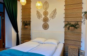 Zemlinsky Hof, © Wiener Alpen Ein gemütliches Schlafzimmer mit einem Doppelbett, dekorativen Wandteppichen und Pflanzen.