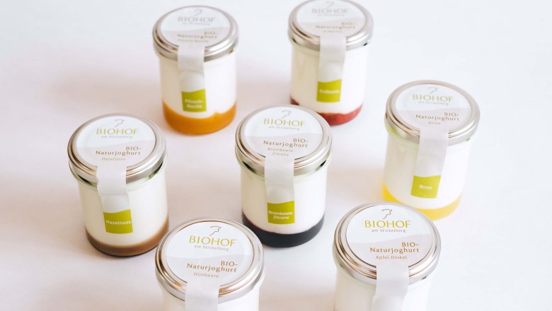 Yogurt organic farm at Stickelberg, © Anni Lechner Fotografie Seven glasses of natural yoghurt, each with different fruit toppings, against a white background.