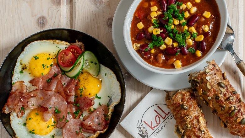 Hot snacks, © Koll GmbH Various hot snacks on a table, including fried eggs with bacon, chili con carne, sandwiches and rolls.