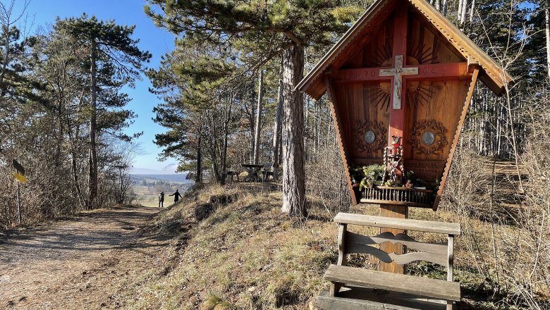 Blickplatz Rotes Kreuz, © Wiener Alpen/Katharina Lechner Holzkreuz mit Bank in einem Waldgebiet, sonniger Tag.