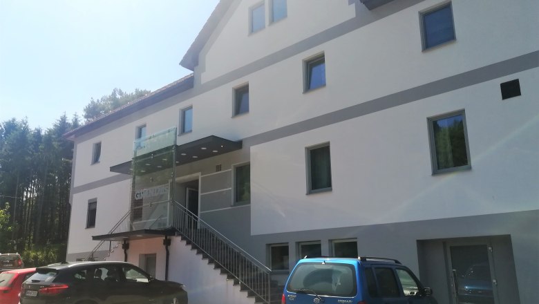 Gasthaus Grandits, © Wiener Alpen Außenansicht eines modernen Gasthauses mit mehreren Fenstern und parkenden Autos davor.