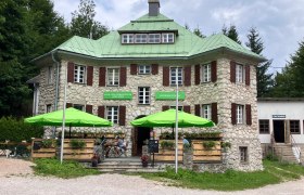 Naturparkstüberl, © Naturpark Hohe Wand Steingebäude mit grünem Dach und Sonnenschirmen vor dem Eingang.