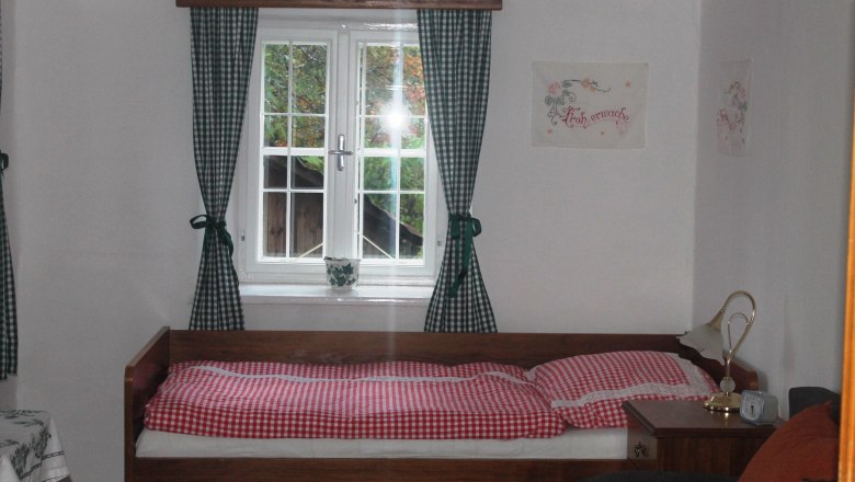Ferienwohnung Fam. Holzer, © Familie Holzer Gemütliches Schlafzimmer mit Einzelbett, kariertem Bettzeug und grün-weiß karierten Vorhängen.