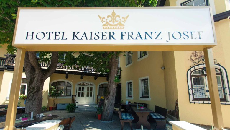 Garten Hotel Kaiser Franz Josef, © Hotel Kaiser Franz Josef Eingang des Hotel Kaiser Franz Josef mit Schild und Bäumen.