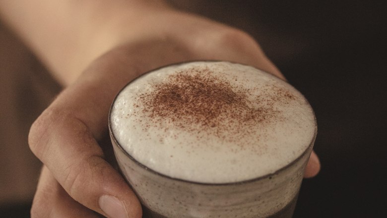 Dorfstetter bakery, © Bäckerei Dorfstetter Close-up of a hand holding a glass with cappuccino and milk foam.