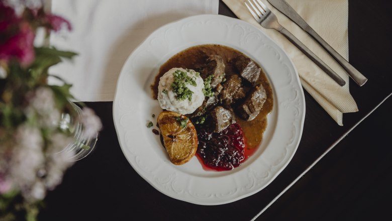 Pub classic: venison stew, dumplings, cranberries, © Niederösterreich-Werbung/Sophie Menegaldo A plate with venison ragout, dumplings, cranberries and a fried slice of lemon.