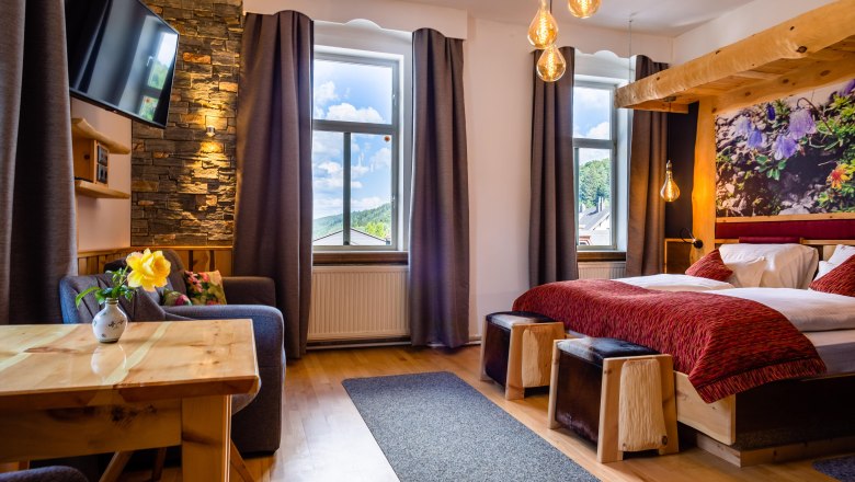 Doppelzimmer, © Scharfegger´s Raxalpen Resort Gemütliches Doppelzimmer mit Holzmöbeln, einem Bett, Sofa, Tisch und großen Fenstern mit Vorhängen.
