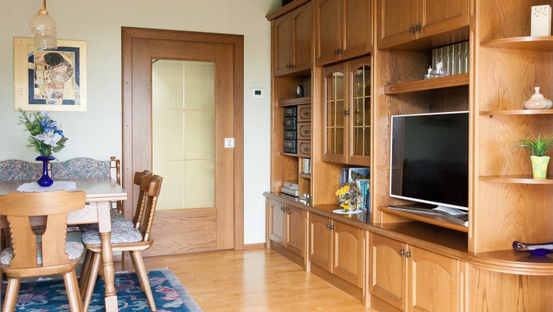 Wohnzimmer, © Fam. Sulzbacher Ein traditionelles Wohnzimmer mit Holzmöbeln, einem Esstisch, Stühlen und einem Fernseher.