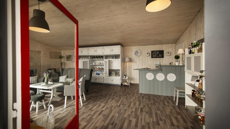 Info- & Genuss-Tankstelle Hochneukirchen, © Marktgemeinde Hochneukirchen / Stefan Knittel Innenansicht eines gemütlichen Cafés mit Holzboden, weißen Möbeln und dekorativen Elementen.