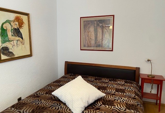 Schlafzimmer, © Wiener Alpen Ein Schlafzimmer mit einem Bett, zwei gerahmten Bildern an der Wand und einem roten Nachttisch.