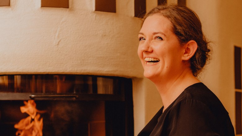 Wirtin Eva Maria Reisenbauer, © Niederösterreich Werbung/Klaus Engelmayer Frau lächelt vor einem Kamin mit brennendem Feuer.