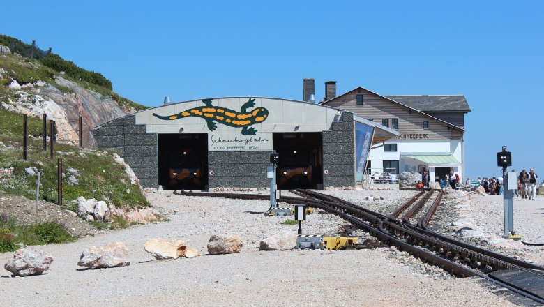 Berghaus Hochschneeberg, © Niederösterreichische Schneebergbahn GmbH, Foto Franz Zwickl Eingang der Schneebergbahn mit Salamander-Logo und Berghaus im Hintergrund.