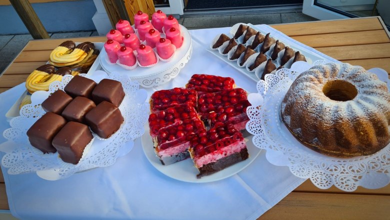 Hausgemachte Mehlspeise, © Stadtcafé Gloggnitz Verschiedene hausgemachte Mehlspeisen auf einem Tisch, darunter Gugelhupf, Schokoladenwürfel und Kirschkuchen.