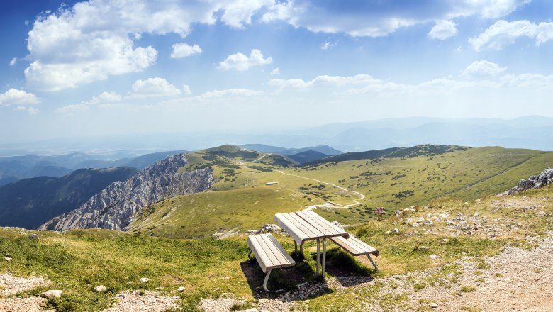 Blickplatz Fischerhütte Schneeberg, © Wiener Alpen, Foto: Franz Zwickl Panoramablick von einem Berg mit einer Bank im Vordergrund und grünen Hügeln im Hintergrund.
