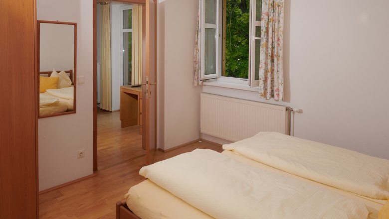 Schlafzimmer, © Landhaus Puchbergerhof by smc Ein Schlafzimmer mit einem Doppelbett, einem offenen Fenster mit Vorhängen und einem Spiegel an der Wand.