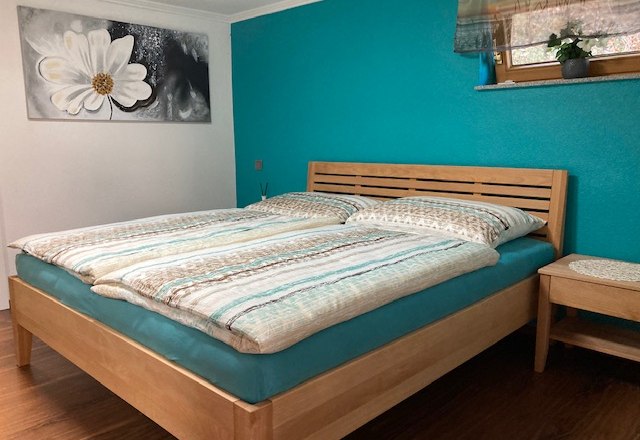 Schlafzimmer, © Thomas Ruzicka Schlafzimmer mit Doppelbett, türkisfarbener Wand und Blumenbild.