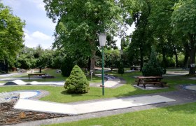 Minigolf Wiener Neustadt, © Minigolf Wiener Neustadt Minigolfplatz mit Bäumen und Bänken in einem Park.