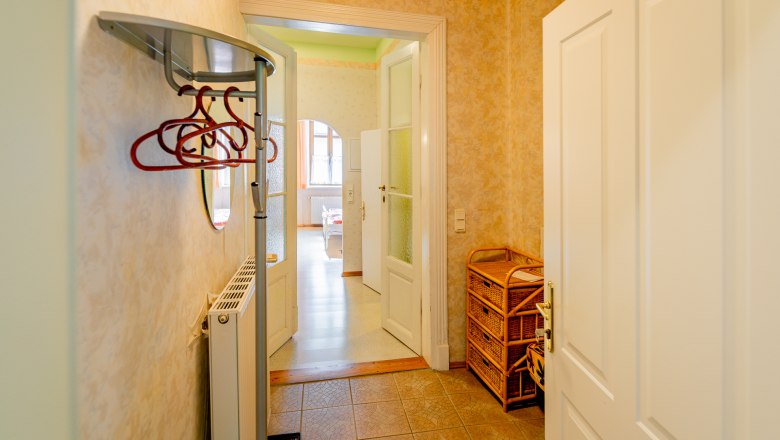Anteroom, © Wiener Alpen /Christian Kremsl An anteroom with coat hooks, a radiator and wicker furniture. A door leads into a bright room with windows.
