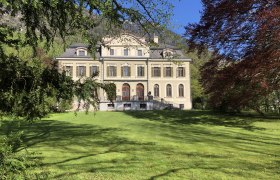 Herrnhof, © Herrnhof Ein großes, elegantes Herrenhaus mit symmetrischer Fassade und mehreren Fenstern, umgeben von grüner Wiese und Bäumen.