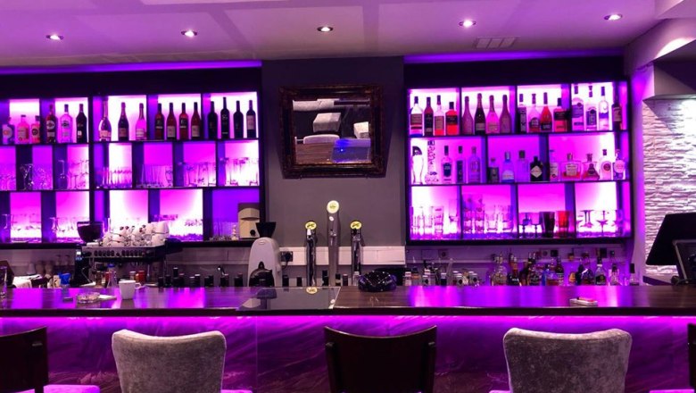 Die Bar, © Elit Facebook Eine stilvolle Bar mit lila Beleuchtung, Flaschenregalen und Sitzplätzen.