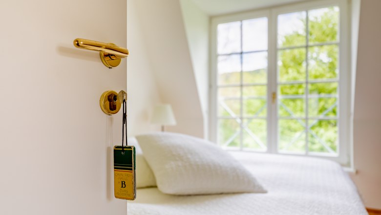 Kavaliershäuser, © Wiener Alpen / Christian Kremsl Offene Tür mit Schlüssel und Schild, dahinter ein Bett und Fenster.