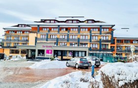 Vivea 4* Hotel Bad Schönau Zur Quelle, © Wiener Alpen Hotelgebäude "Zur Quelle" mit bunter Fassade im Winter und geparkten Autos im Vordergrund.