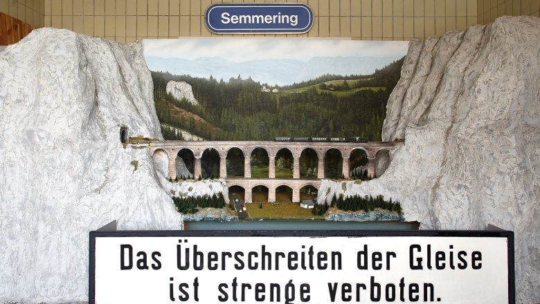 Modell Kalte Rinne-Viadukt, © Wiener Alpen, Foto: Bene Croy Modell des Kalte Rinne-Viadukts mit Zug und Landschaft im Hintergrund. Schild mit Aufschrift: 'Das Überschreiten der Gleise ist streng verboten.'
