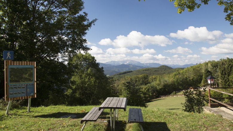 Wanderstartplatz Waxeneckhaus, © Wiener Alpen, Foto: Franz Zwickl Picknicktisch mit Blick auf bewaldete Hügel und Berge, blauer Himmel mit Wolken.