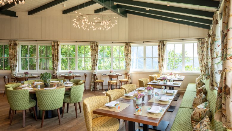 Wintergarten, © Knappenhof Christian Husar Ein heller Wintergarten mit gedeckten Tischen, grünen Stühlen und großen Fenstern.